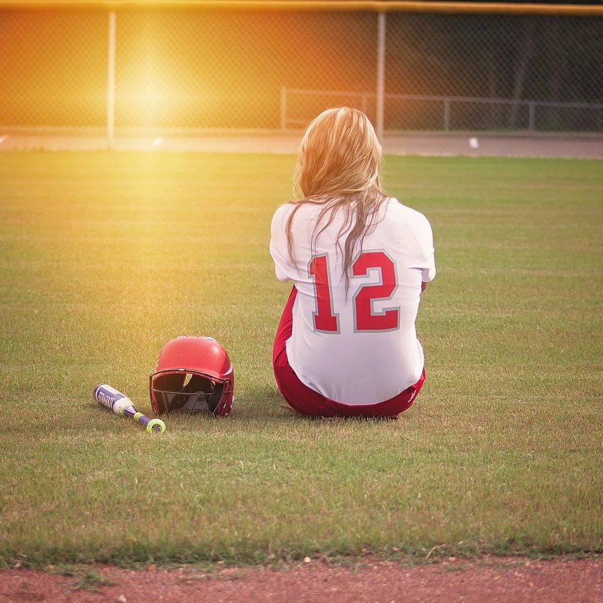 softball picture of kid sitting down staring at the sunset.